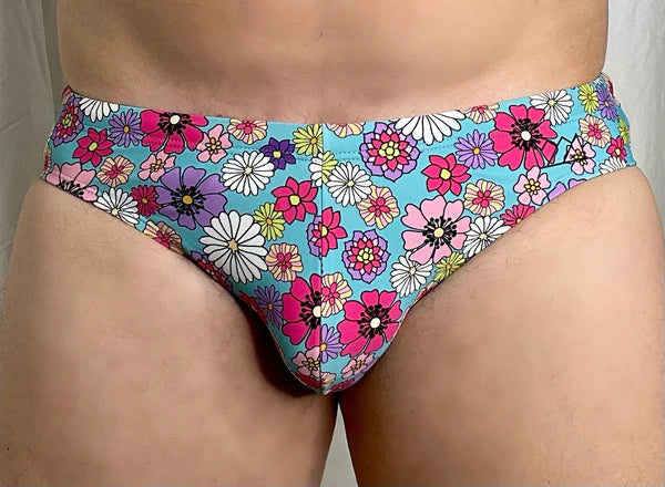 Brightly colored turquoise floral-patterned men’s swim briefs by Chris Turk featuring pink purple white and yellow flowers