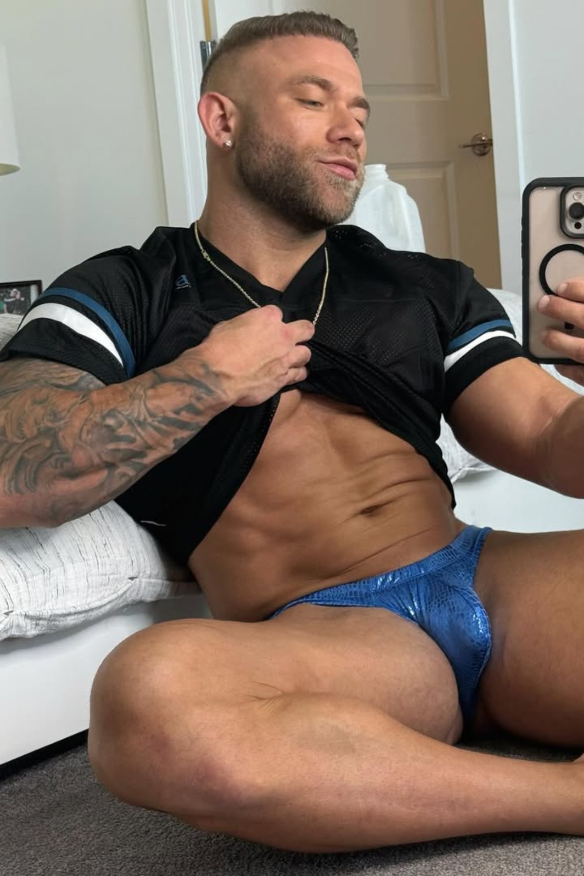 Man in black athletic jersey and blue metallic briefs, showcasing physique.