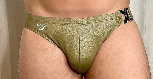Olive green glittery swim briefs with black buckle and white logo near waistband featured in heavy metal glitter line