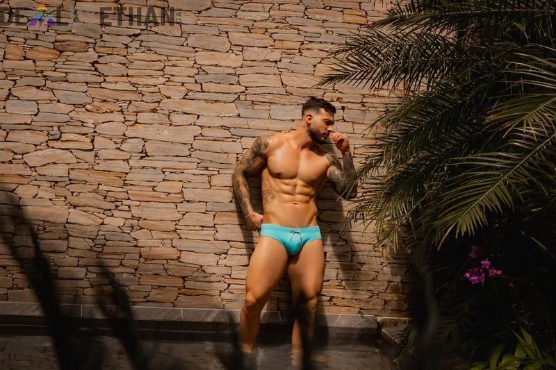 A man wearing bright turquoise swim trunks with a drawstring waistband in pride swimwear collection.