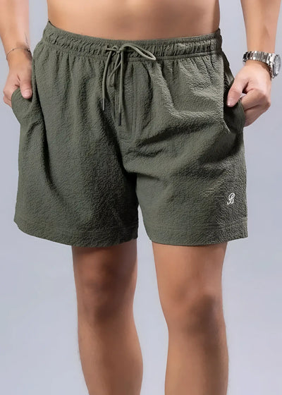 Olive green textured shorts with drawstring waist, worn by model, grey background.