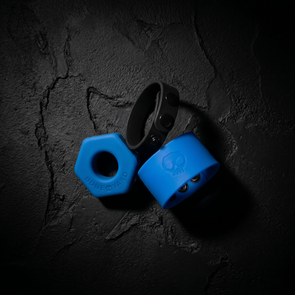 Boneyard Toys silicone collection — blue hex cock ring, black cock strap and blue ball strap on dark concrete