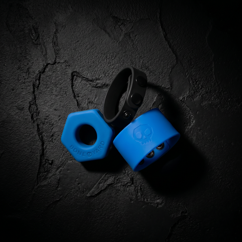 Boneyard Toys silicone collection — blue hex cock ring, black cock strap and blue ball strap on dark concrete
