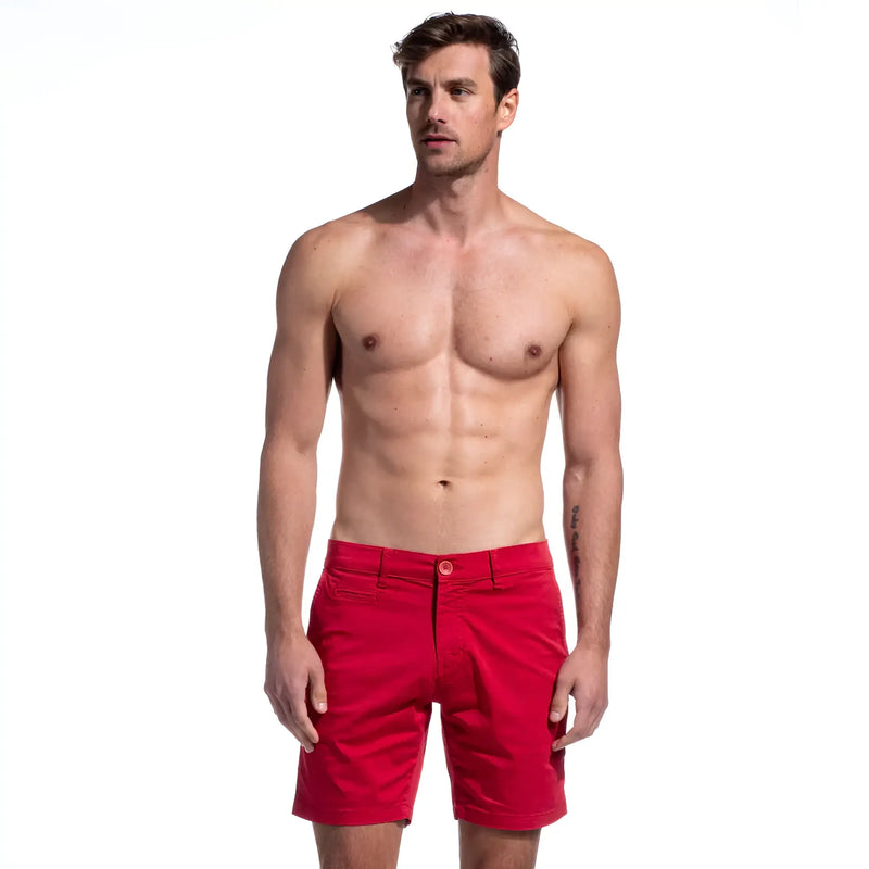 Shirtless man standing against a white background wearing bright red shorts.