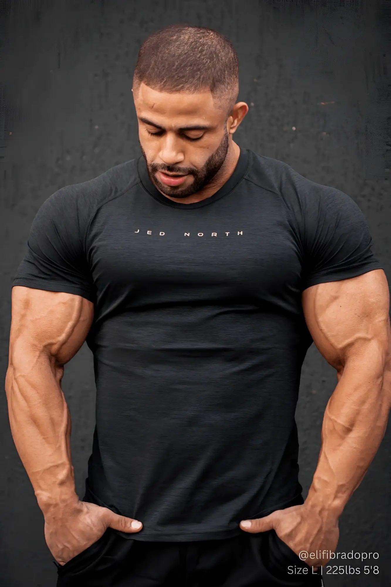 Muscular man wears a fitted black heathered crewneck tee against dark background.