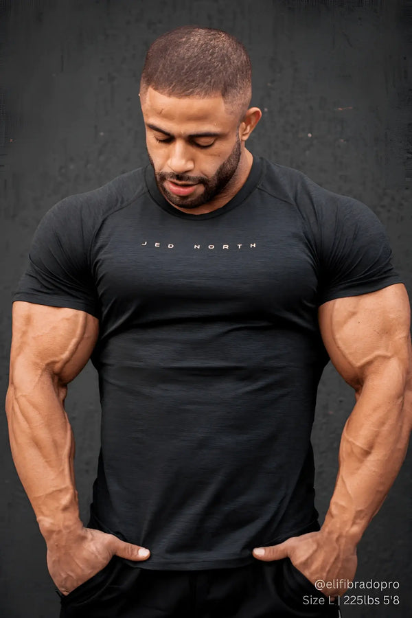 Muscular man wears a fitted black heathered crewneck tee against dark background.