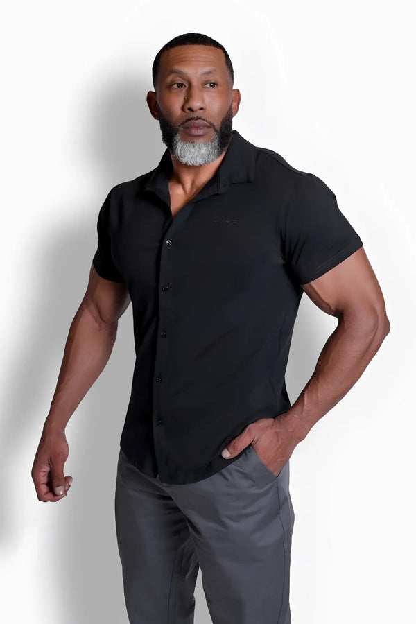 Muscular man wearing a black short-sleeved button-down shirt and grey trousers.