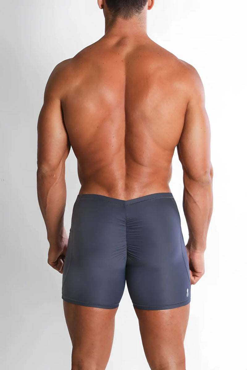 A muscular man wears dark gray bike shorts with a vertical back ruching.