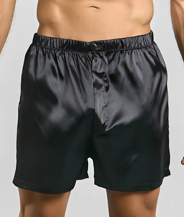 Black satin boxers with elastic waistband and single button on gray background.