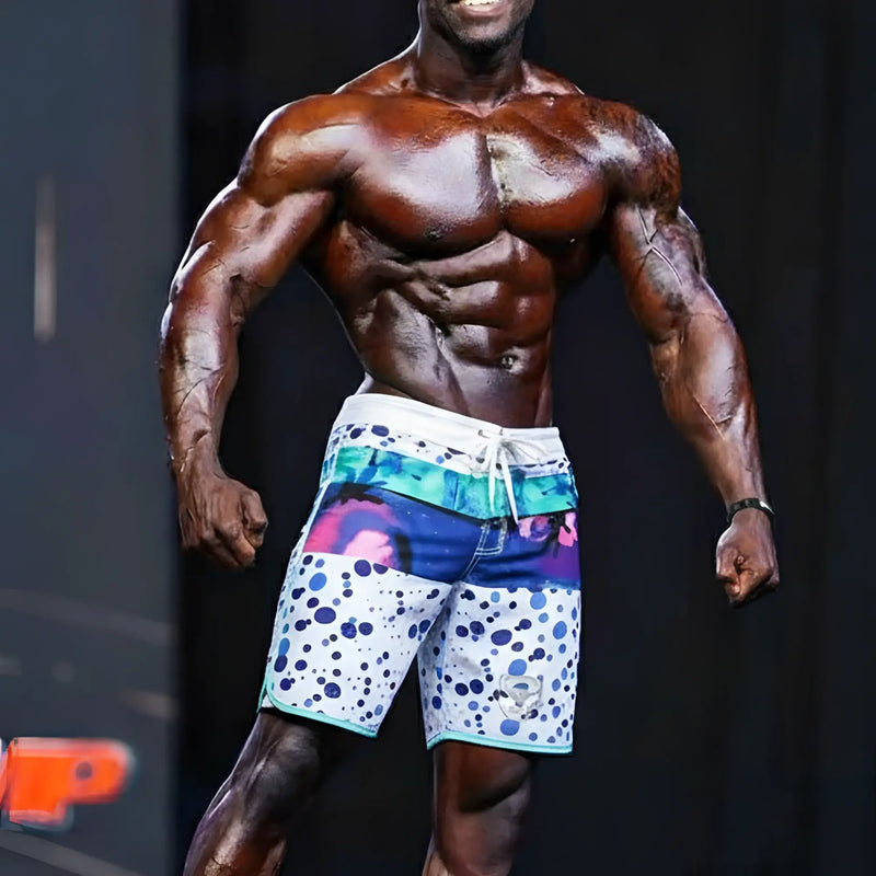 Muscular athlete wears polka-dot and abstract print board shorts on stage.