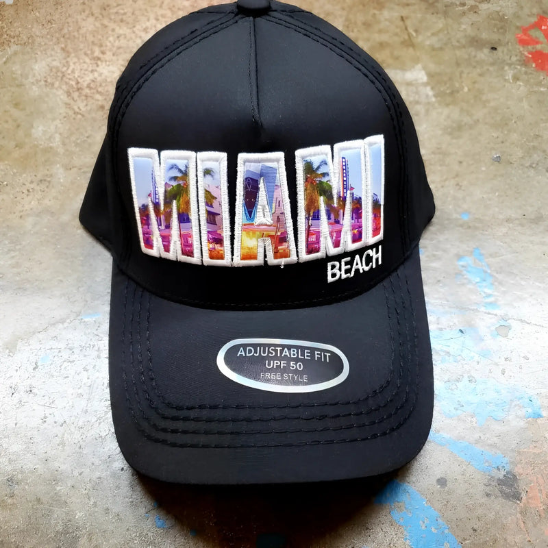 Black baseball cap with Miami Beach text graphic on textured stone surface.