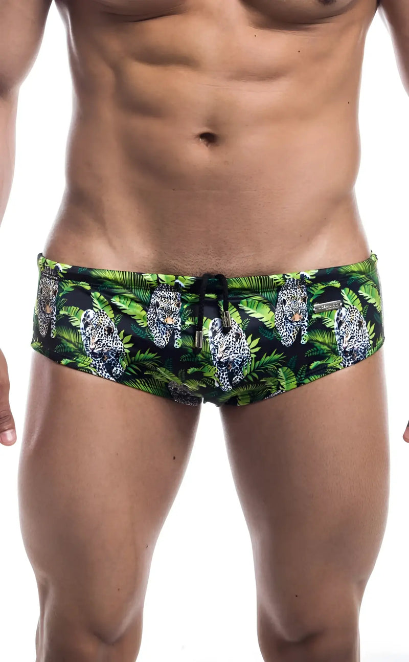 Muscular man wears leopard print swim briefs against a plain white background.