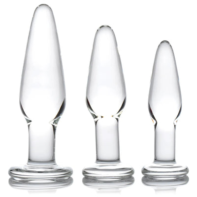 Three clear glass anal plugs of varying sizes stand against white background.