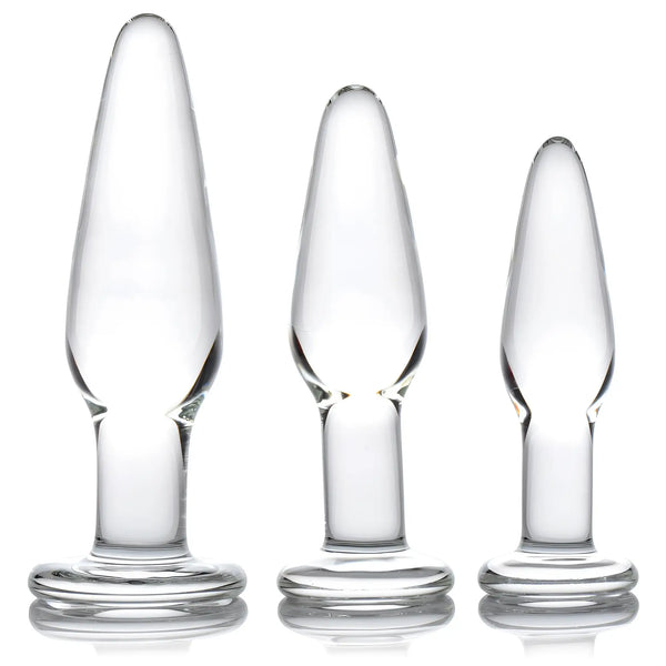Three clear glass anal plugs of varying sizes stand against white background.