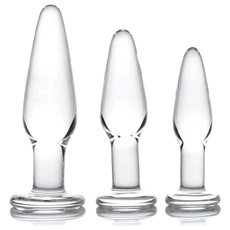 Three clear glass anal plugs of varying sizes stand against white background.