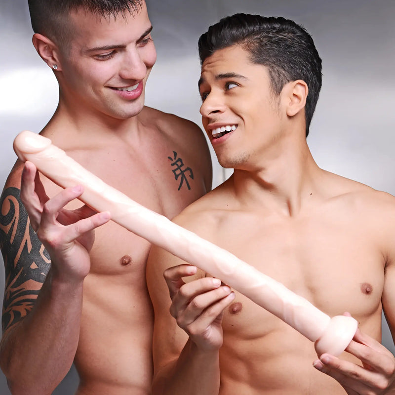 Two shirtless men hold a long, smooth, light-colored object against gray backdrop.