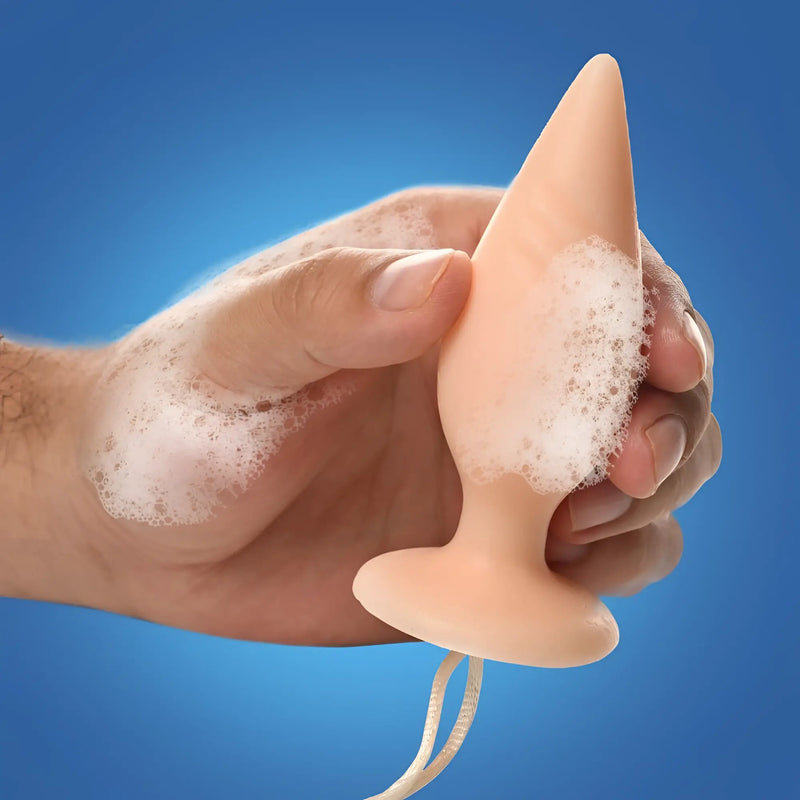 A human hand holds a smooth beige cone object covered in suds.