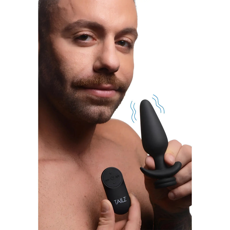 A bearded man holds a black silicone object and small remote control.