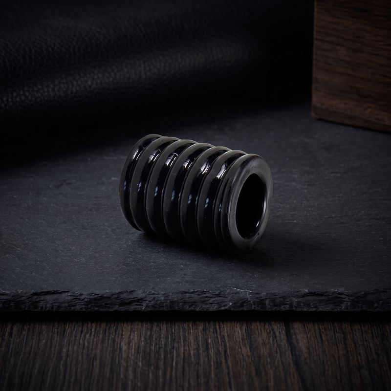 Black mens intimate accessory presented on a white studio background, appearing sleek and sculptural.