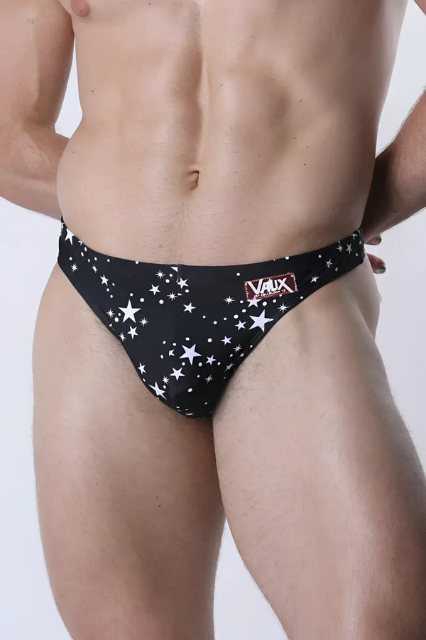 A man wears black star-print briefs against a plain white studio background.