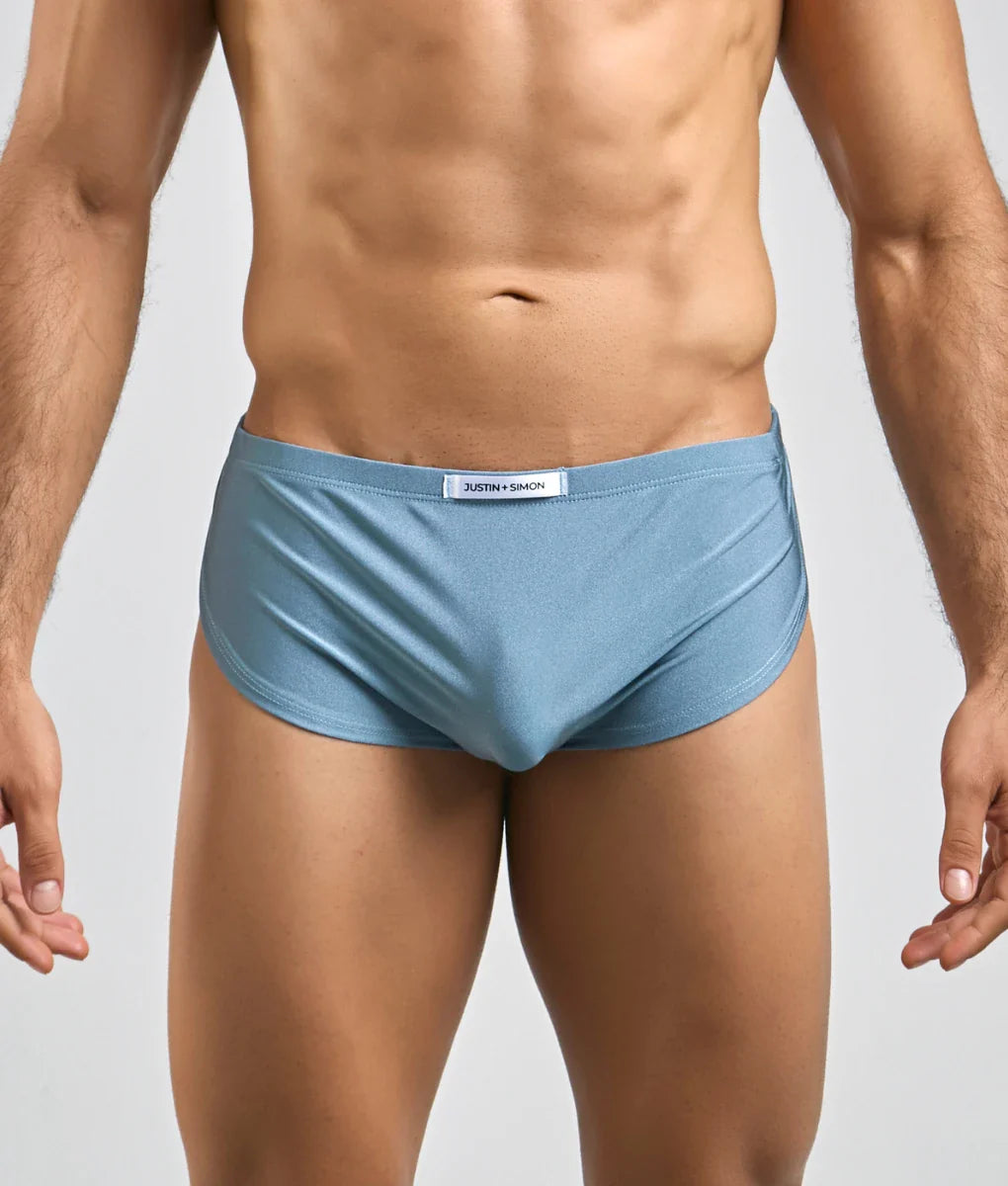 Light blue form-fitting Justin + Simon running briefs with subtle sheen and white brand tag at the waistband