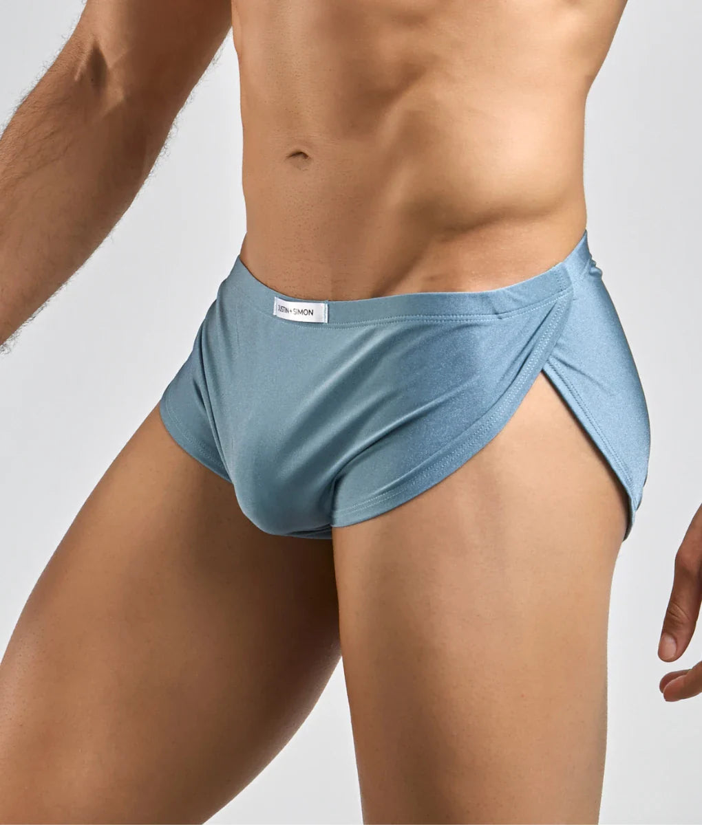 Light blue smooth textured men’s briefs with elastic waistband and subtle side slit in justin simon running short style