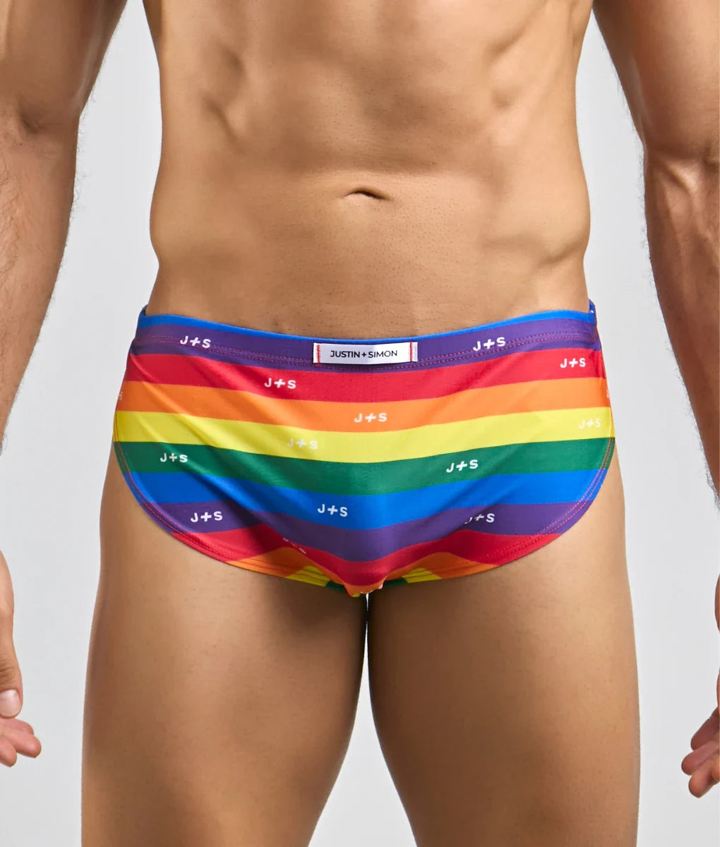 Justin + Simon running short rainbow-striped men’s swim trunks with vibrant colors and repeating j+s branding