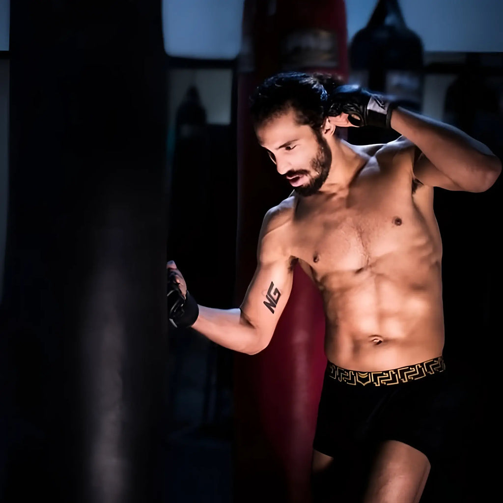 A man wearing black sheath 3.0 modal men’s no fly boxer briefs with gold greek key pattern waistband and boxing gloves