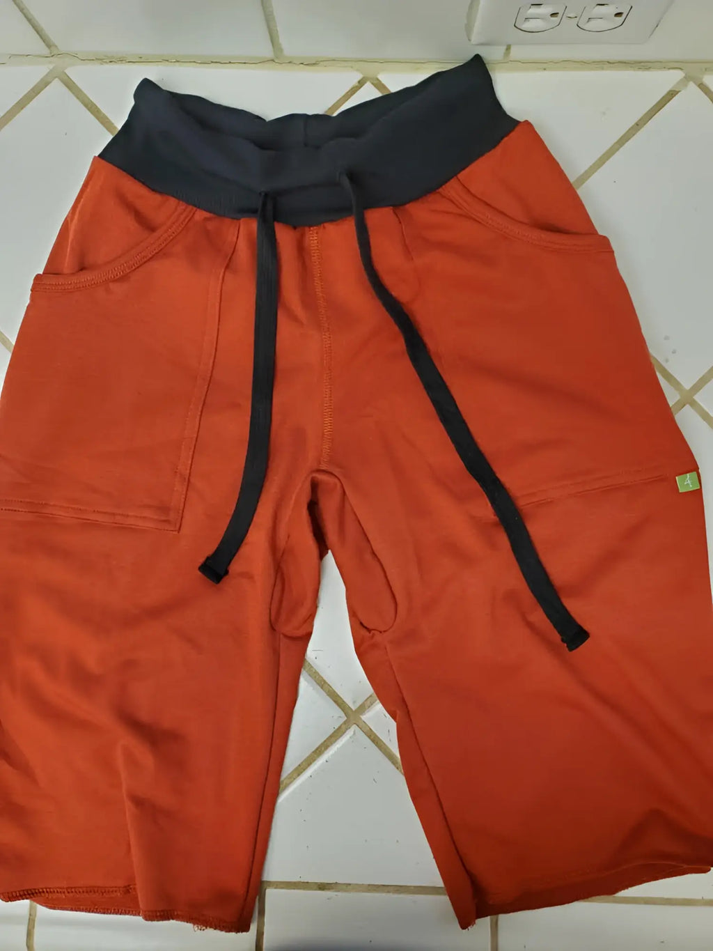 Eco-track short cinnabar orange athletic shorts with black waistband drawstrings side pockets and green brand tag on thigh