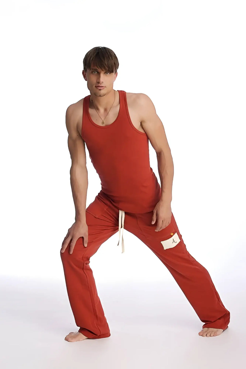 A man wearing cinnabar edge eco-track and yoga sweat pants in red with white drawstrings and a matching red tank top