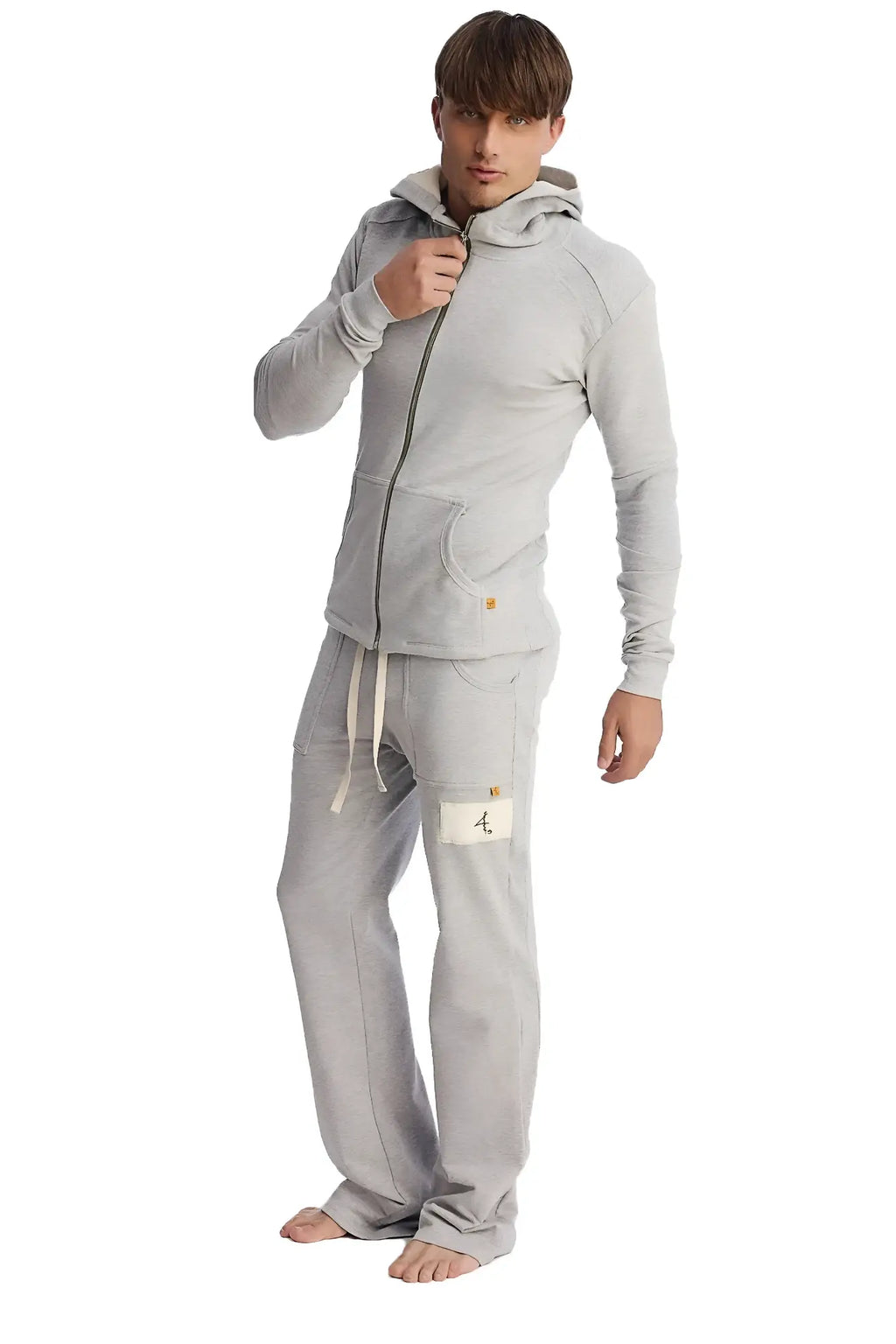 A man wearing heather grey edge eco-track and yoga sweatpants with side pockets and a matching light gray hoodie