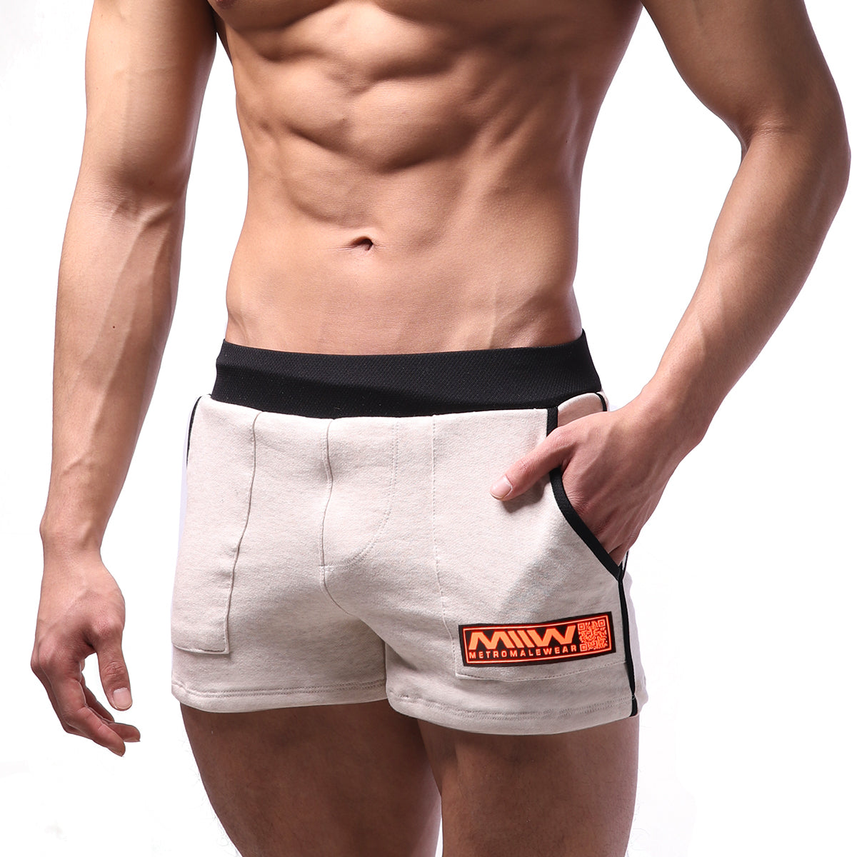Beige cotton metro malewear sport shorts with black elastic waistband and side trim featuring an orange logo patch