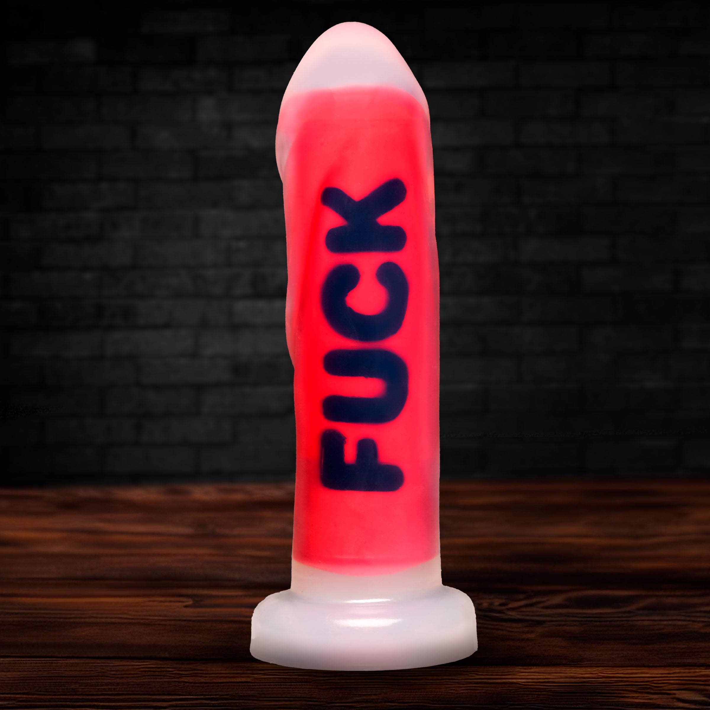 Master Series The Explicit Text silicone dildo in bright red with blue lettering on a wooden surface and brick background.