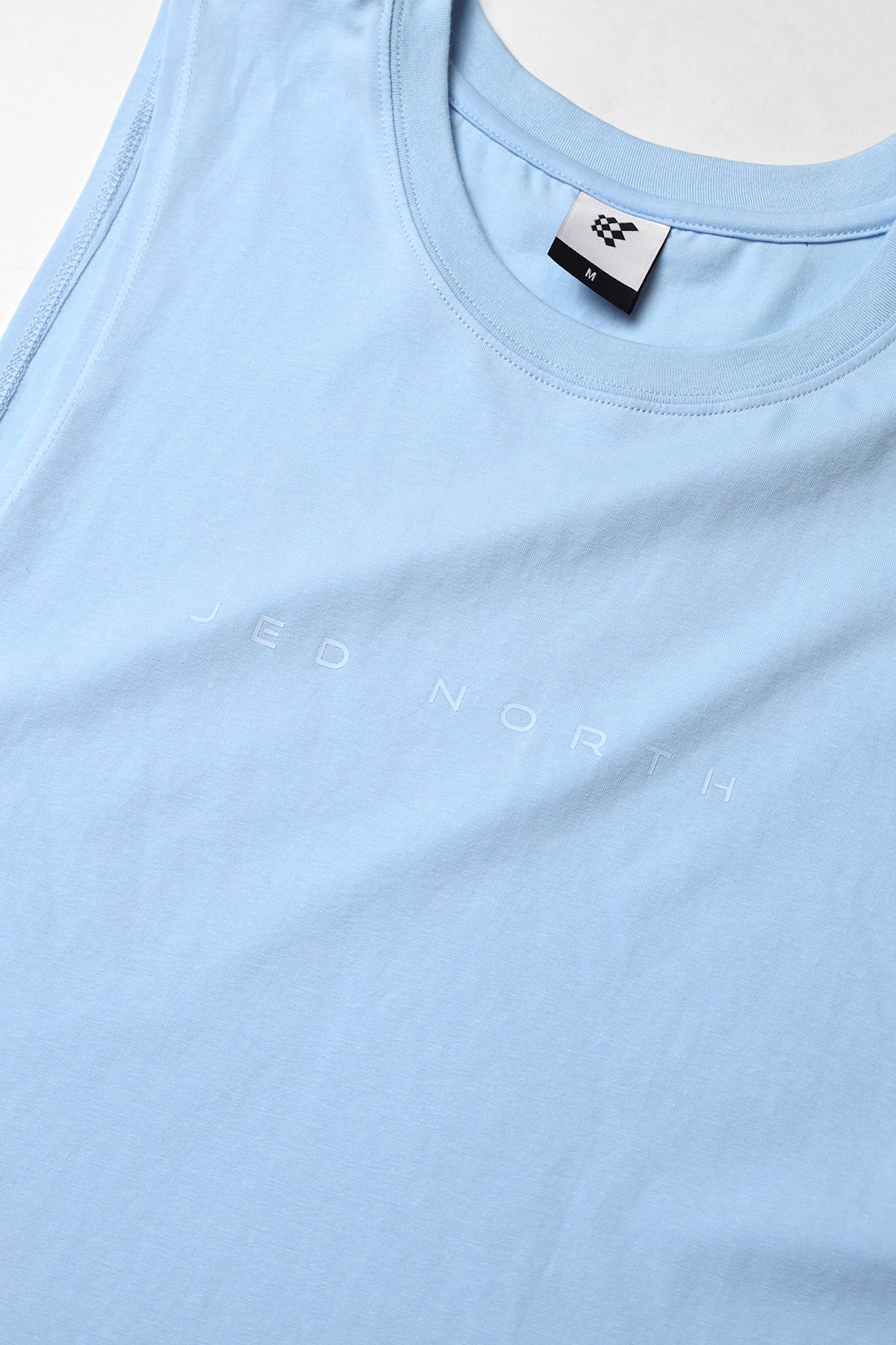 Apollo men’s sleeveless training tee in light blue with subtle jed north lettering and small brand tag at the neckline