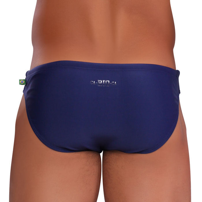 Back view of navy blue bikini cut solids colors sunga men’s swim trunks with brazilian flag tag and bio logo