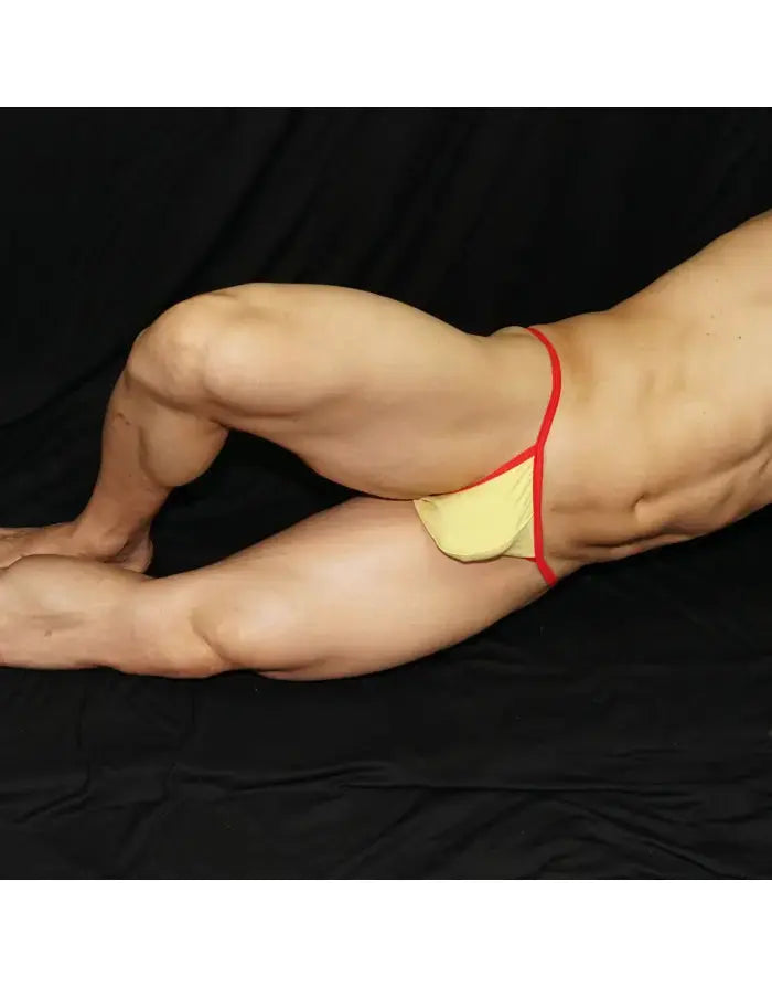 Light yellow men's bikini underwear with red waistband shown on a model in a side pose by Arroyman.