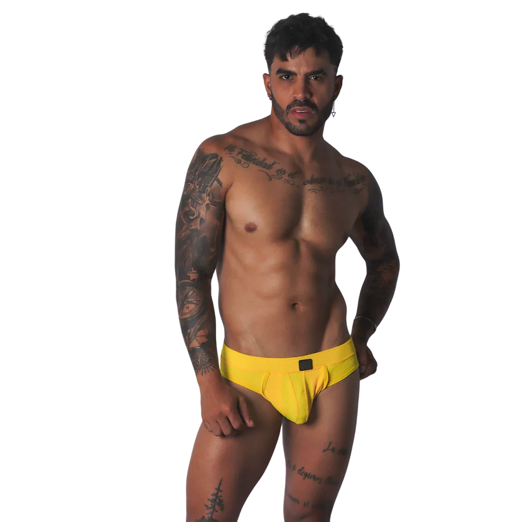 Yellow textured fabric jockstrap with a central black tab detail on the waistband, worn by a tattooed man.