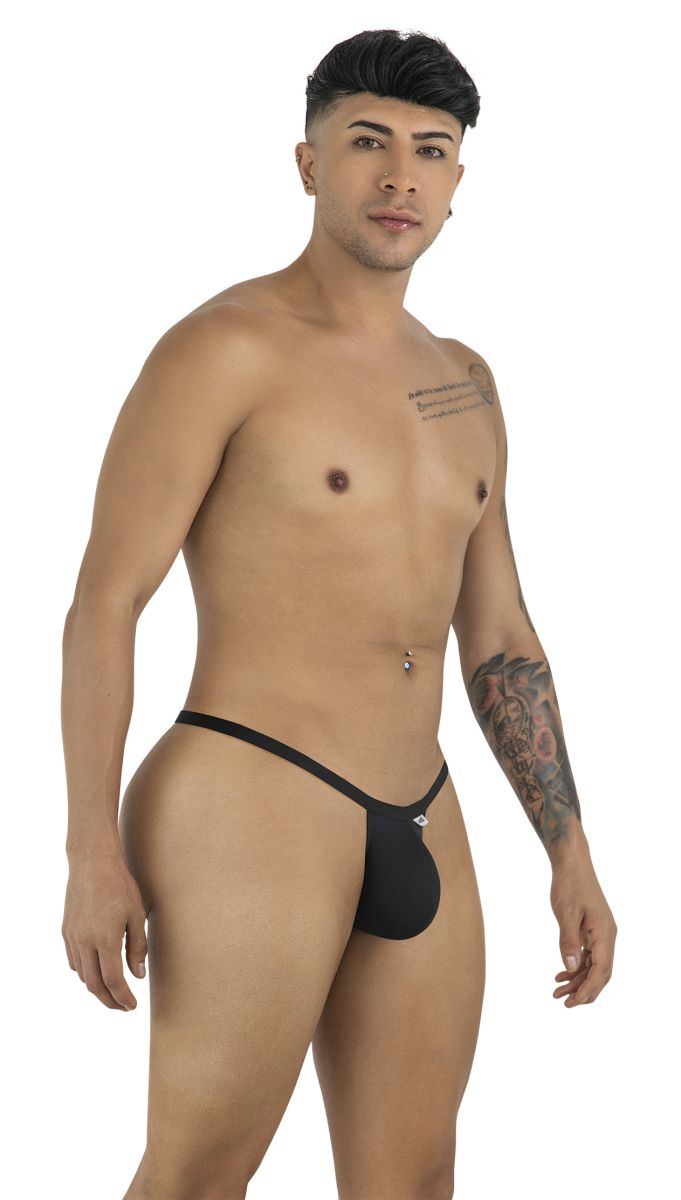 A man with tattoos poses in a minimalist black CandyMan thong, viewed from a side angle against a white background.