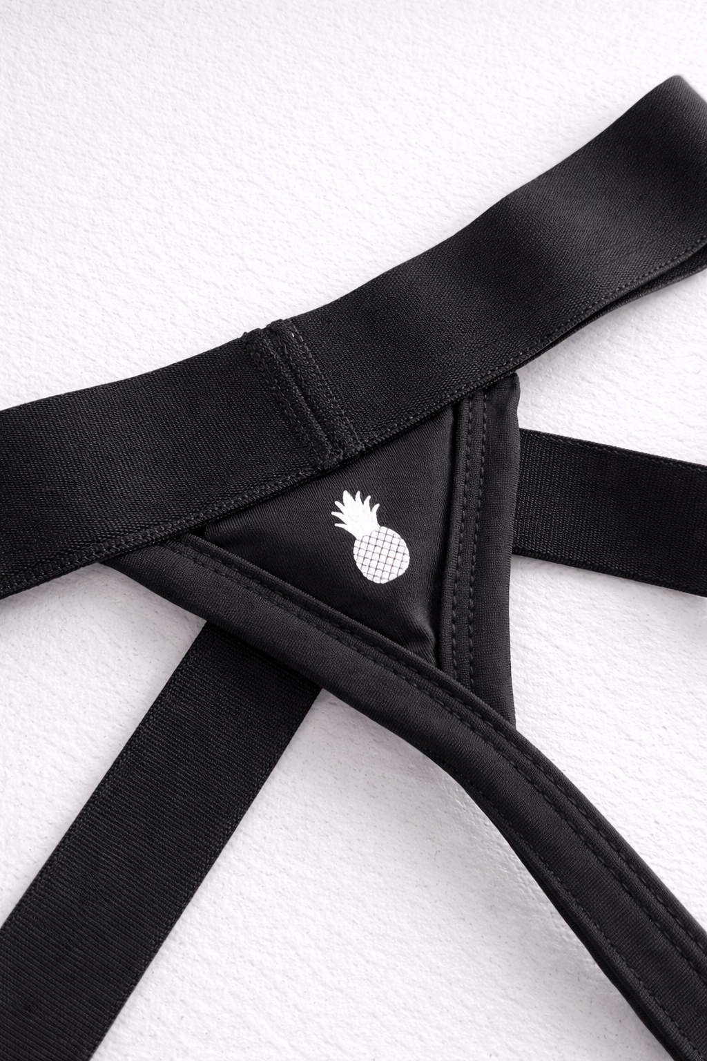 Host-or-travel adjustable jock thong in midnight black with black elastic bandeau and white pineapple emblem