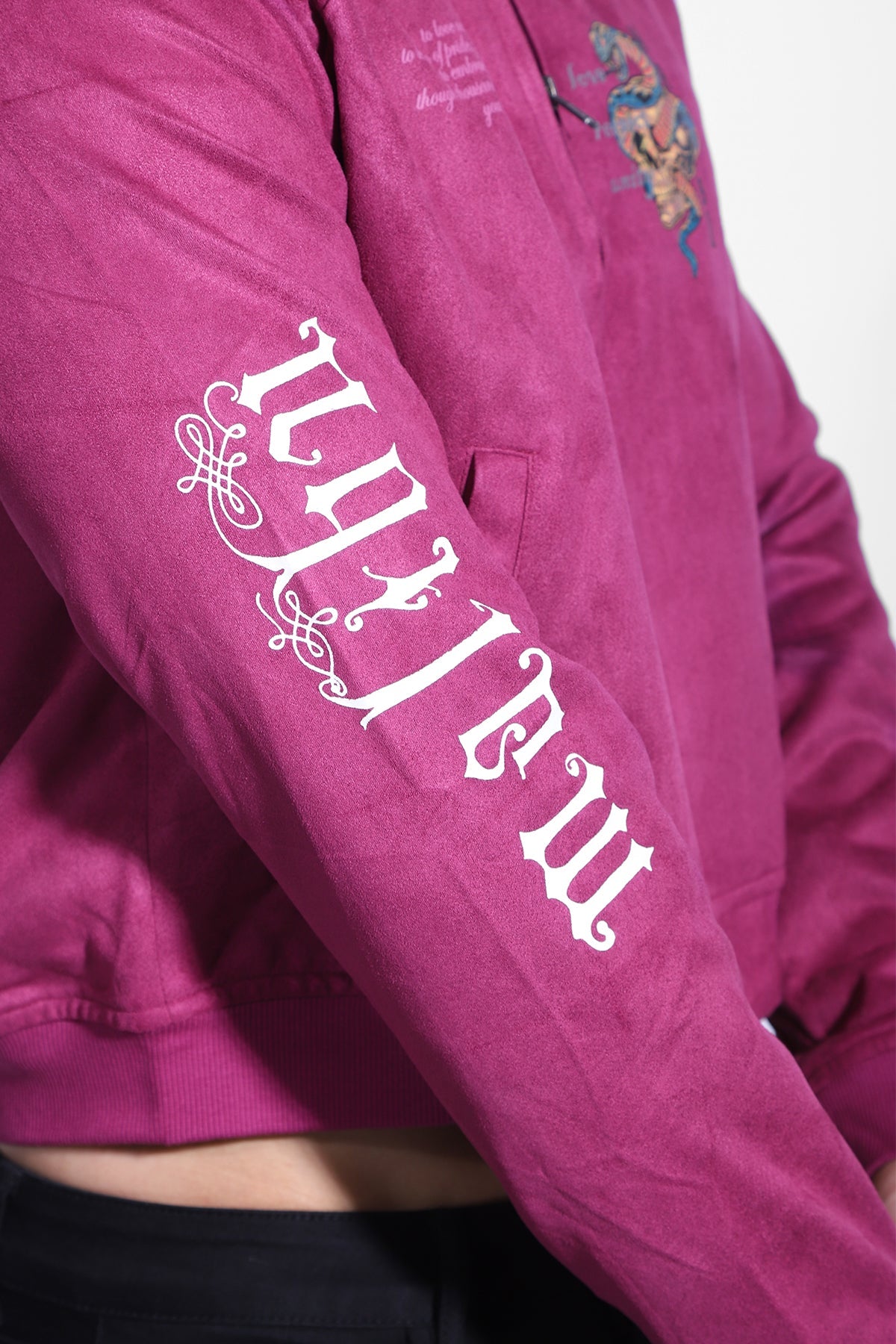 A cropped magenta suede bomber jacket featuring white embroidered lettering and a detailed dragon design on the chest