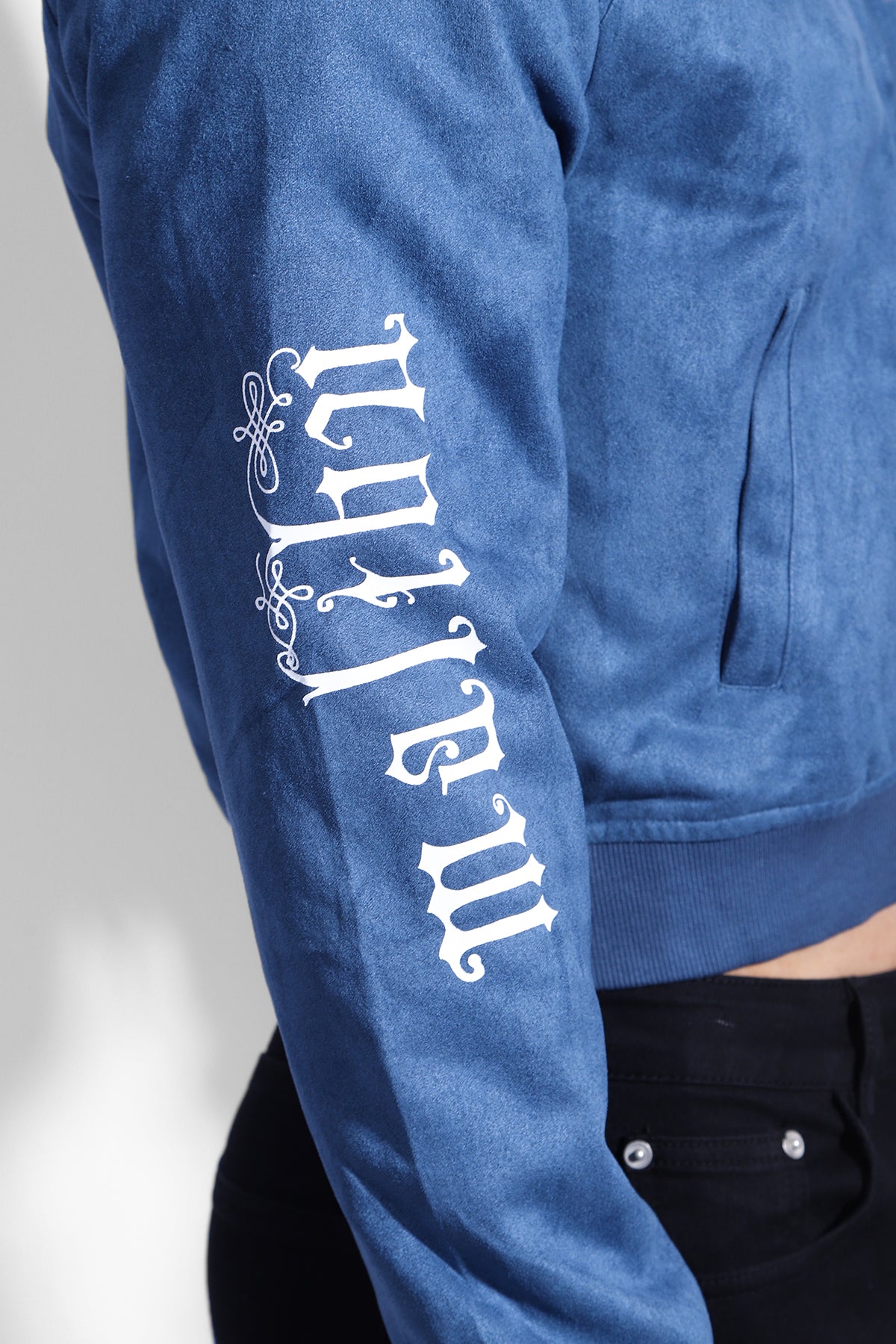 Cropped navy suede bomber jacket with blue suede and white ornate lettering along the sleeve shows the back side