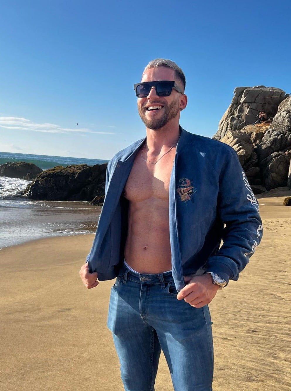 Blue denim jacket with small embroidered patch on left chest and white lettering along the sleeve