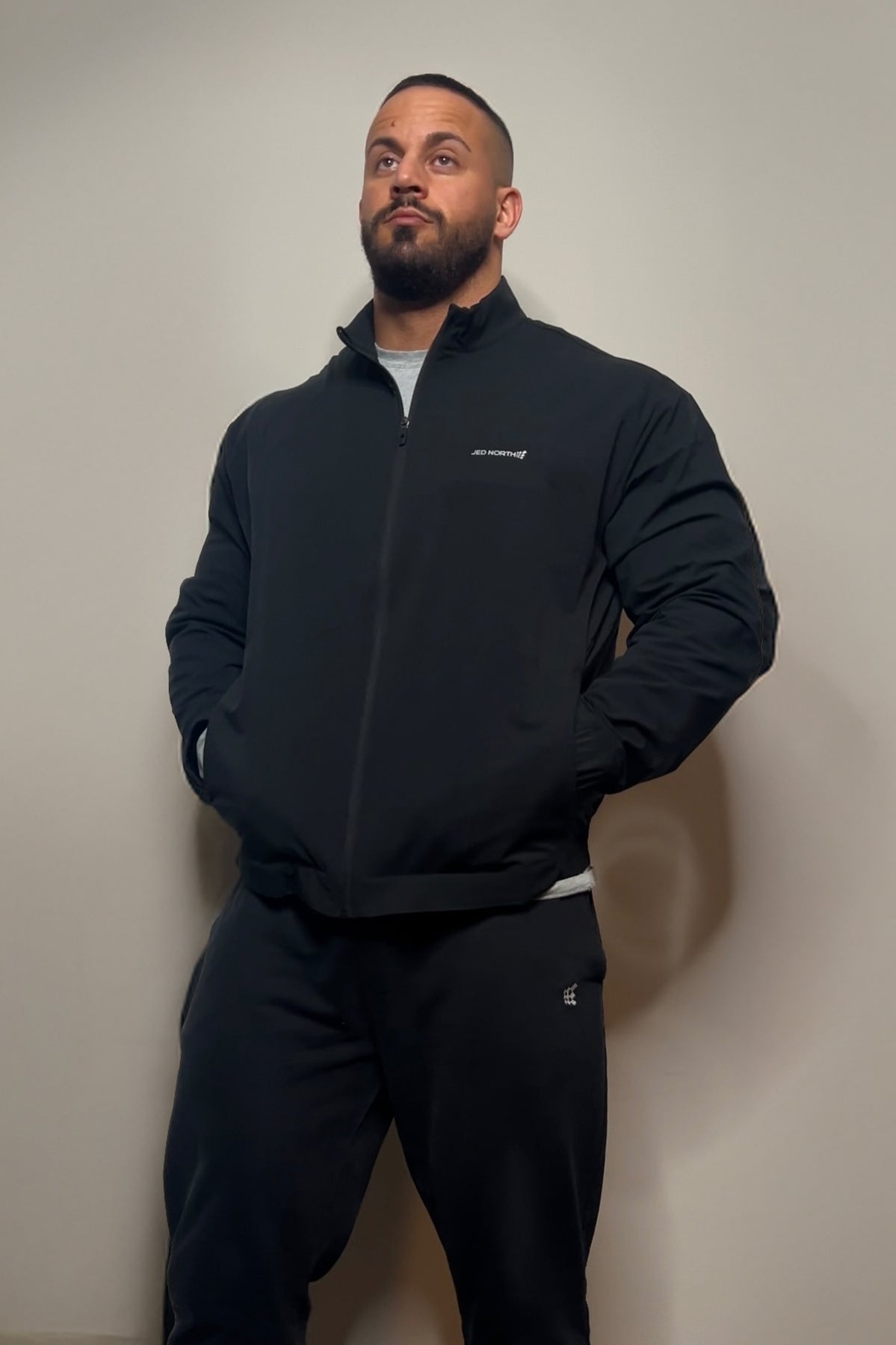 Black full-zip training jacket with subtle white logo on left chest and matching black pants for athletic wear