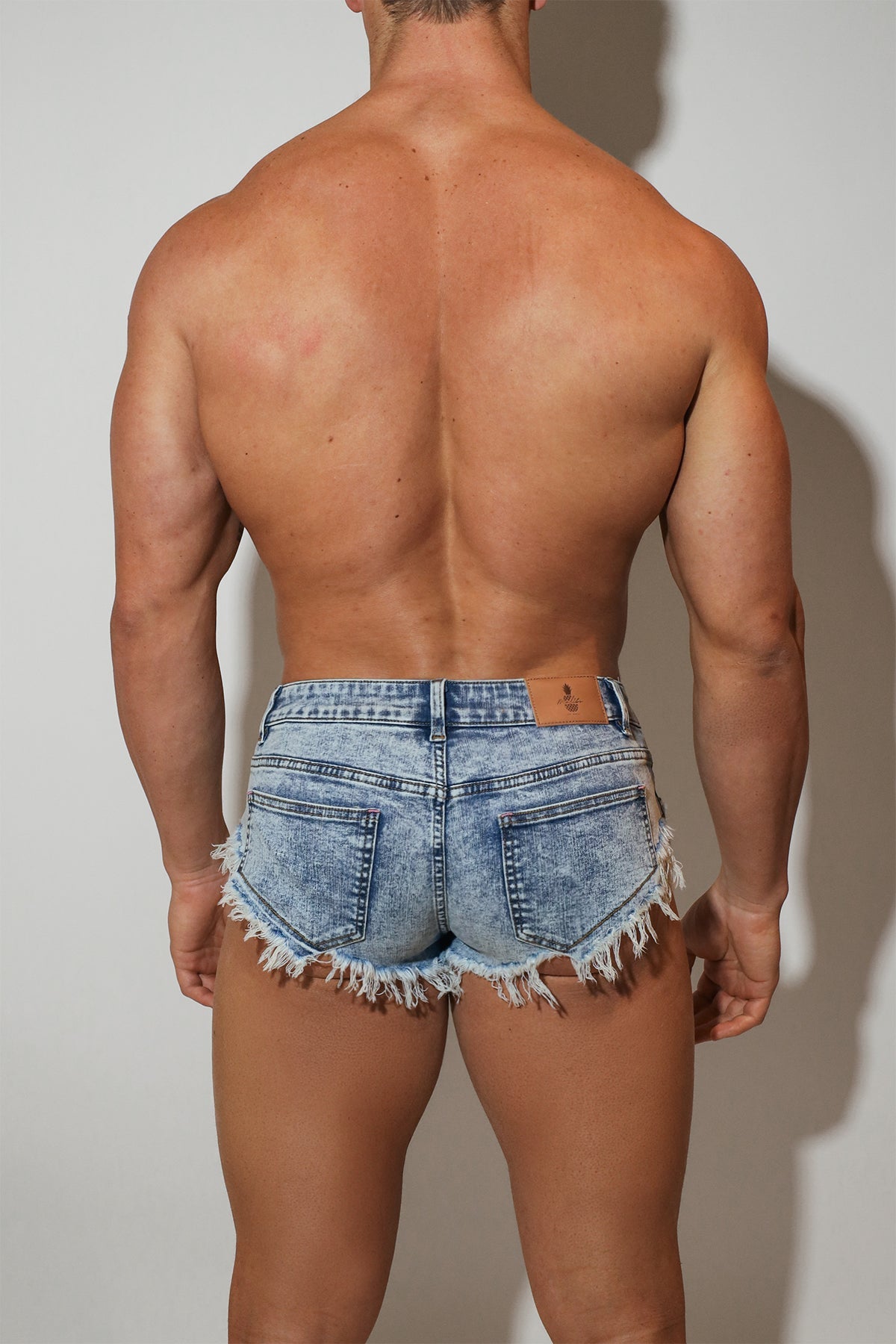 Light-wash acid washed distressed booty shorts with frayed hem and back pockets shown from the back side