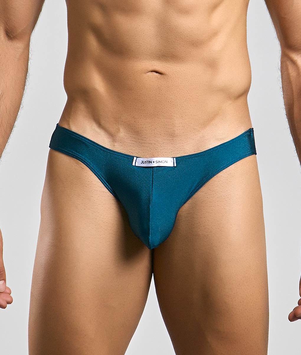 Teal form-fitting mens bikini briefs in smooth fabric with a white justin + simon label on the waistband