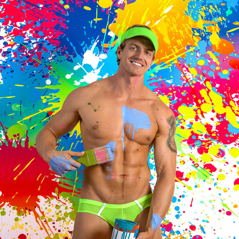 A muscular man wearing neon green kyle kli045 bikini brief swim trunks with matching visor covered in colorful paint splatters