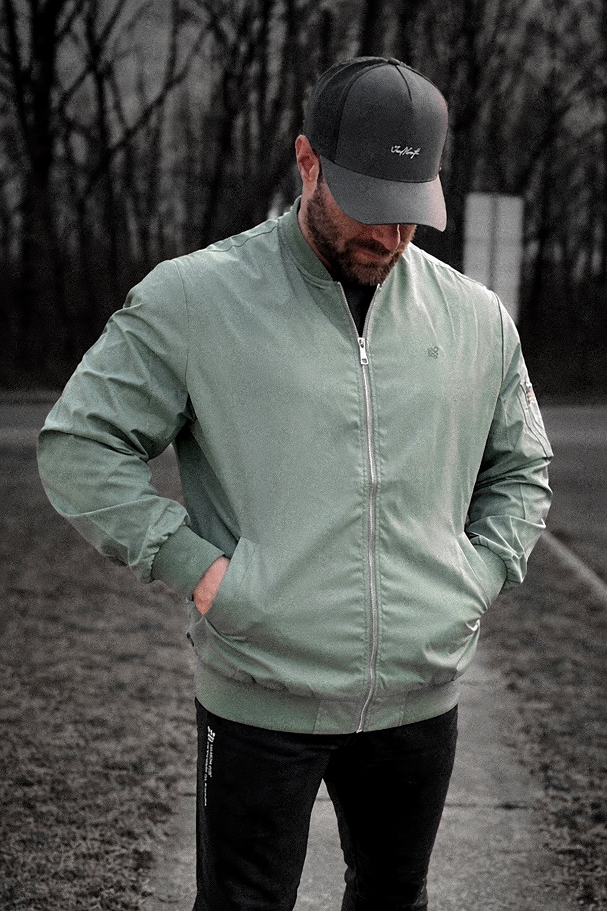 A man wearing a men’s premium olive bomber jacket with zipper front and subtle embroidered chest logo