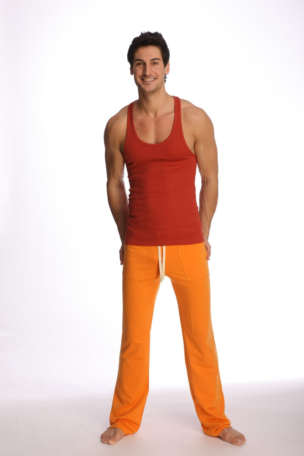 A man wearing a cinnabar racer-back yoga tank in red with orange pants featuring white drawstrings