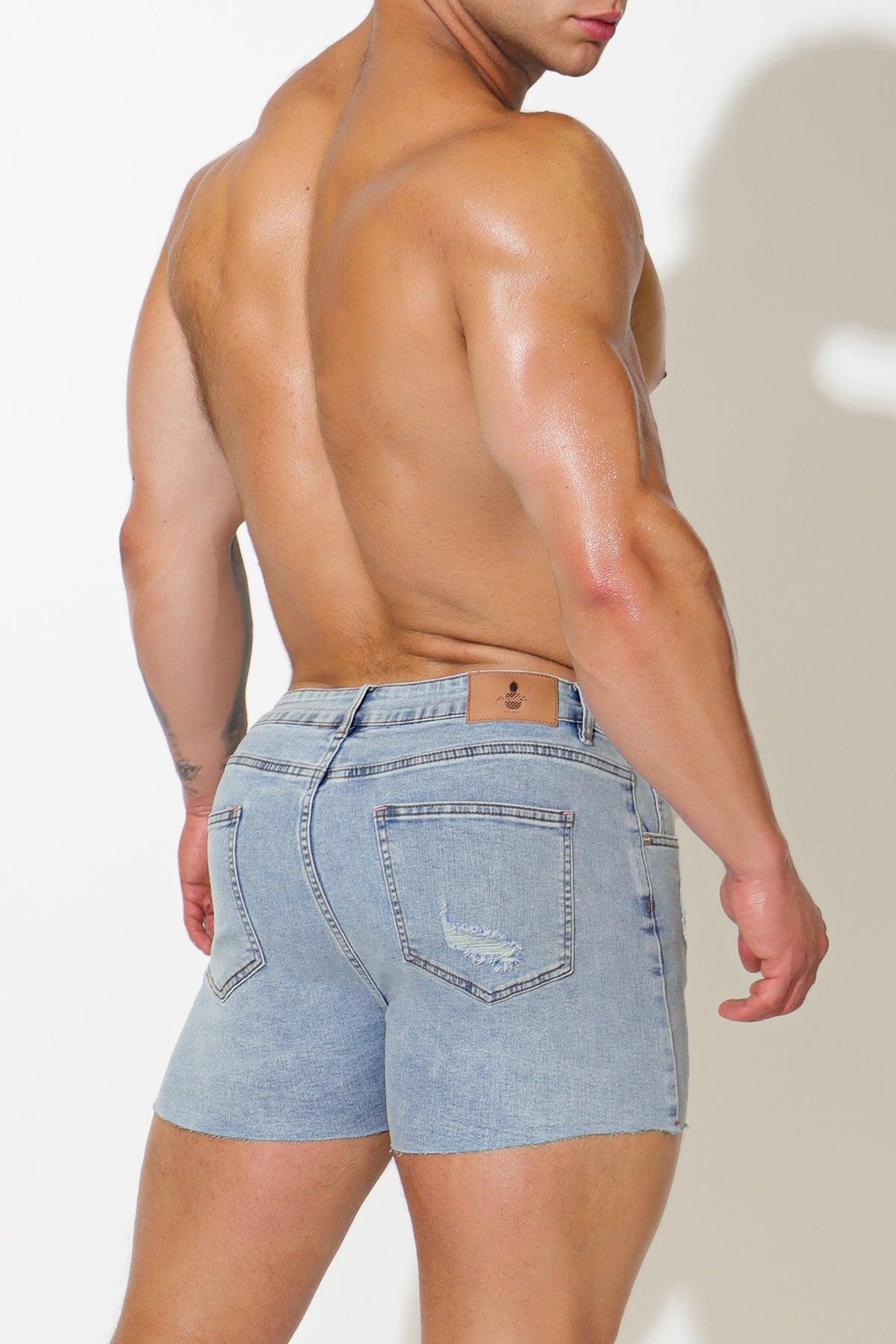 Back side of rockstar raw cut 2.5 inch capri blue light-wash denim shorts with distressed pocket and leather patch