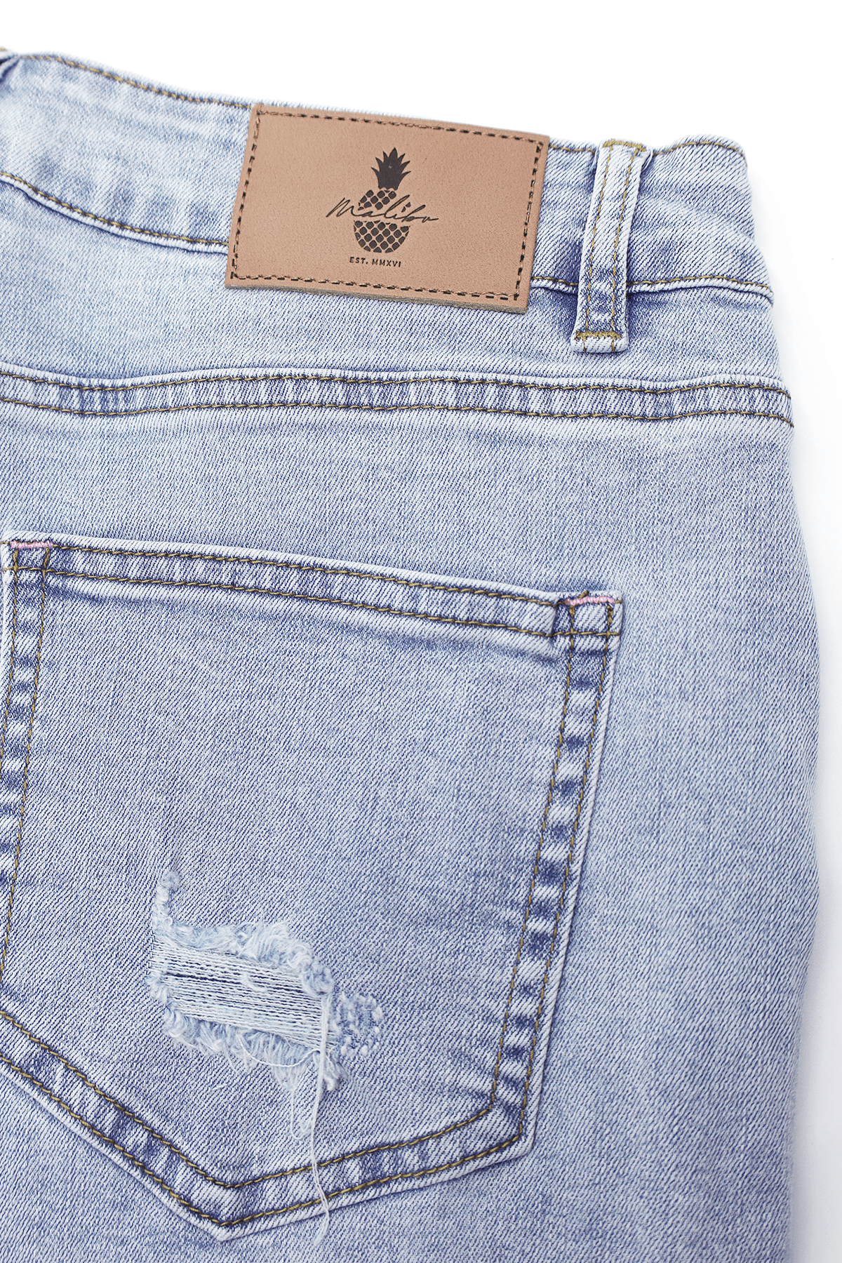 Back of rockstar raw cut 2.5 inch denim short shorts in capri blue with distressed pocket and pineapple leather patch